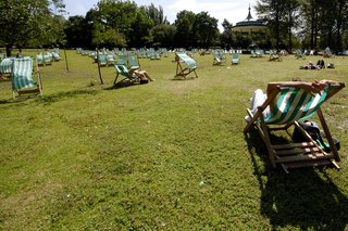 People sitting in deck chairs on the grass in a park on a sunny day