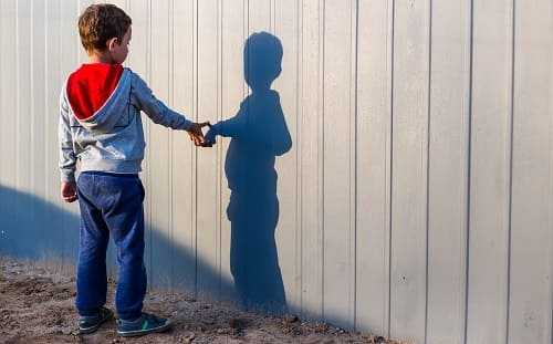 Ребенок играет со своей тенью на заборе